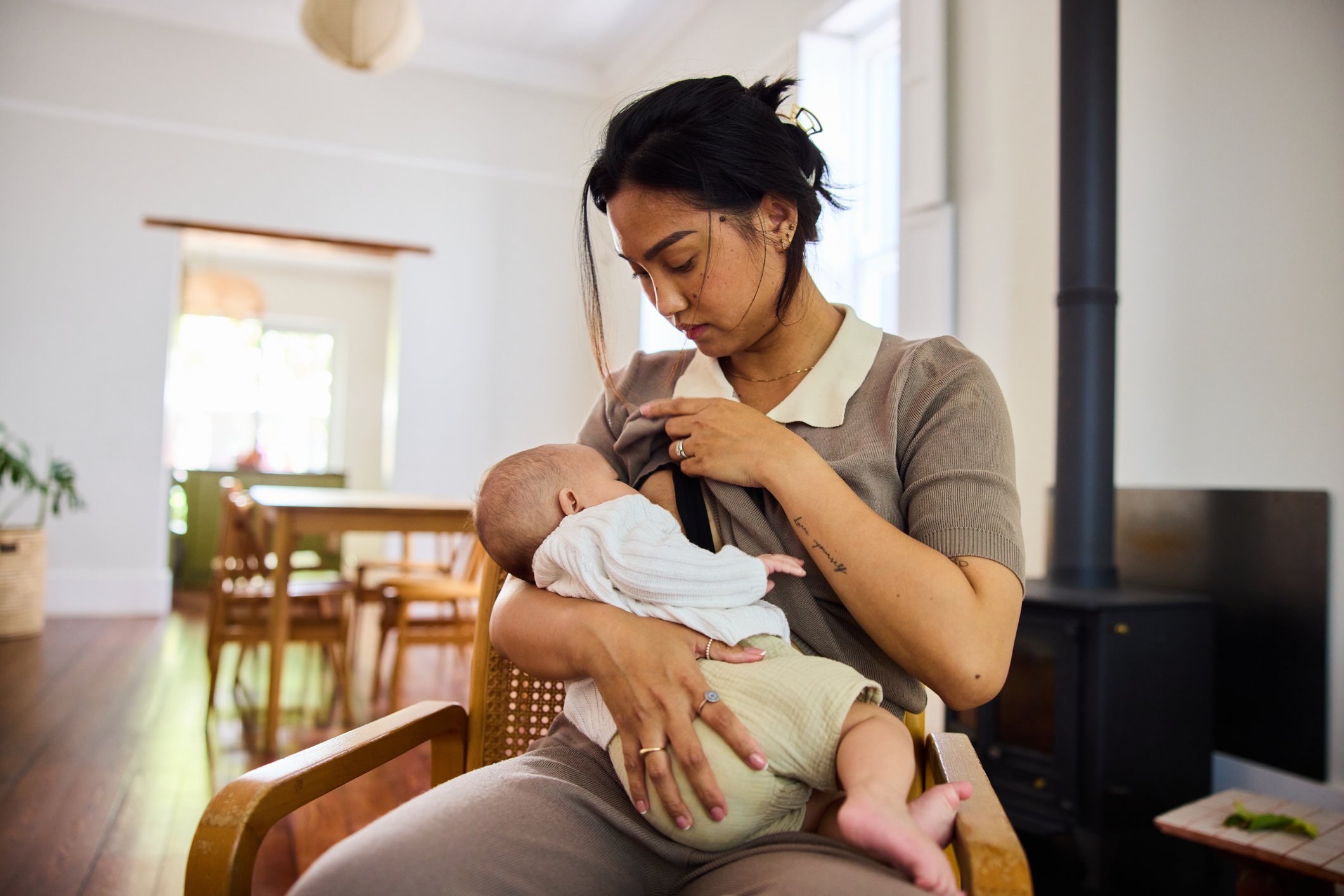 Loving young mother breastfeeding her baby in a bright home interior, holding the baby gently in a moment of tenderness and everyday motherhood.