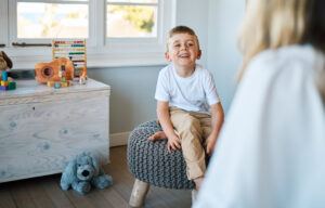 An adorable little boy sitting on a chair while talking to a caucasian therapist. Cute little boy talking to a psychologist. Child checking in with a counsellor at a foster home before being adopted