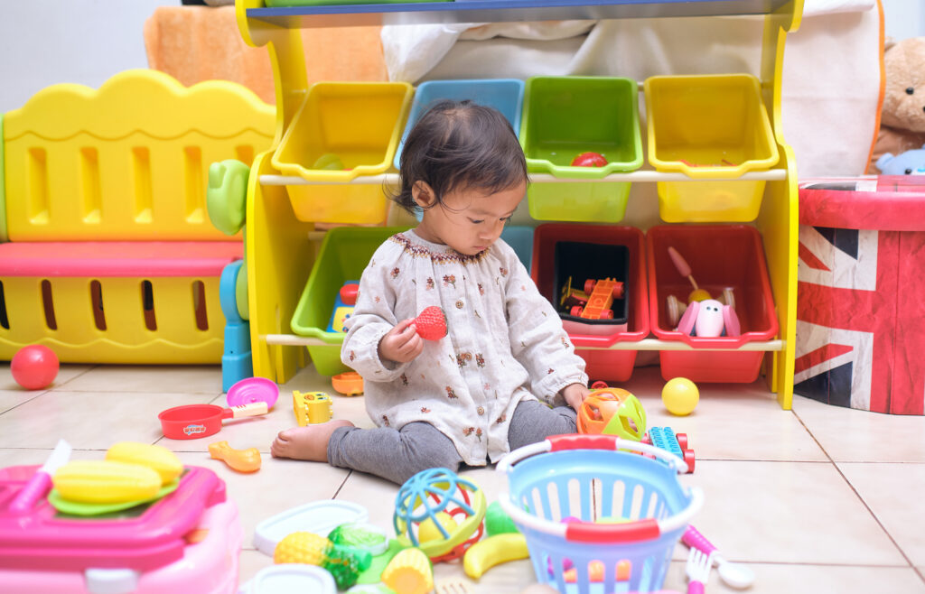 Cute Asian toddler girl child sitting on floor having fun playing alone in playroom at home, Little infant girl sitting W posture which is called W-sitting knees bent and feet positioned outside hips